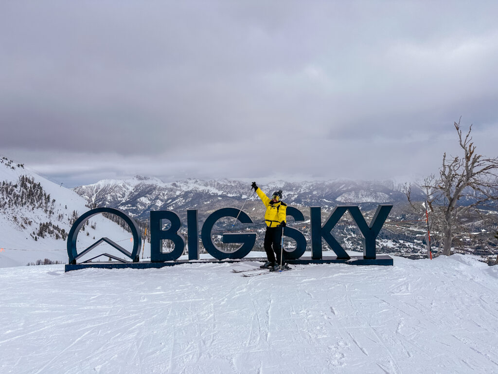Woman standing on mountain in skies in front of Big Sky sign
